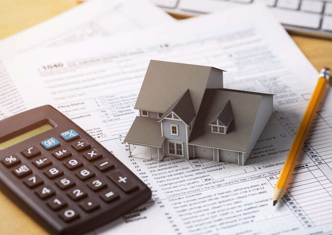 Calculator, pencil, and small model of a home on top of tax forms