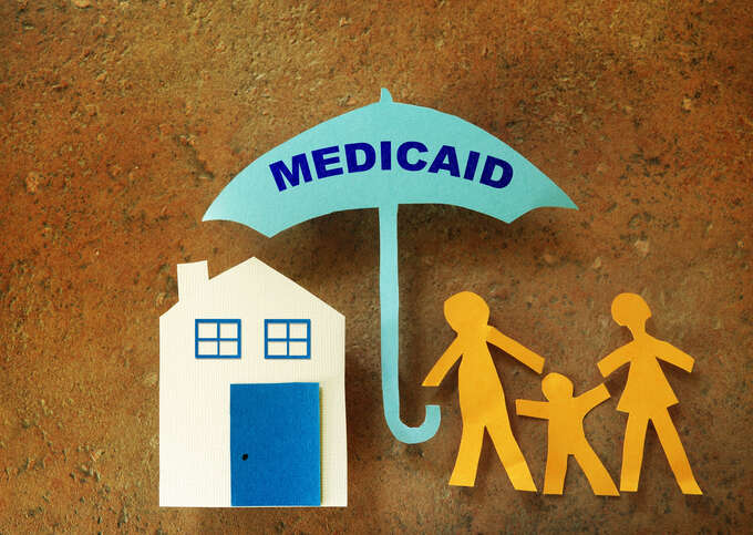 Paper cutouts of house with family holding an umbrella labeled with the word 'Medicaid'