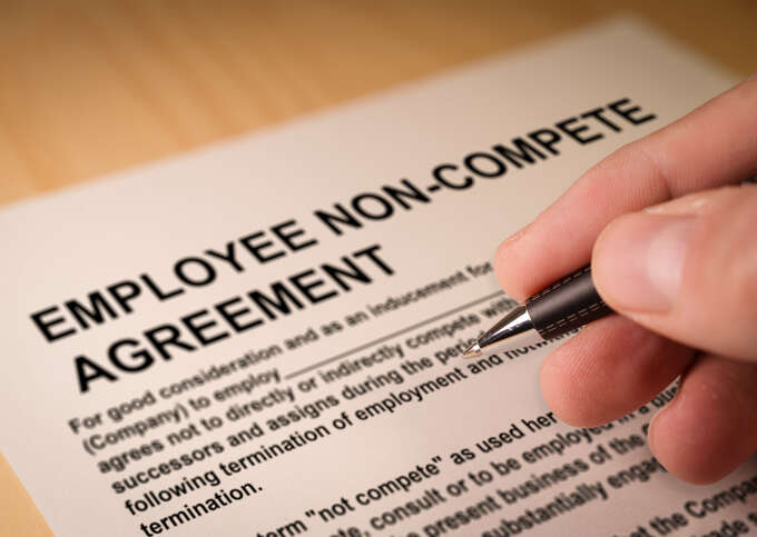 Hand holding pen over employee non-compete agreement document